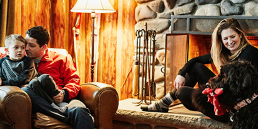 Family relaxing by fireplace in cabin.