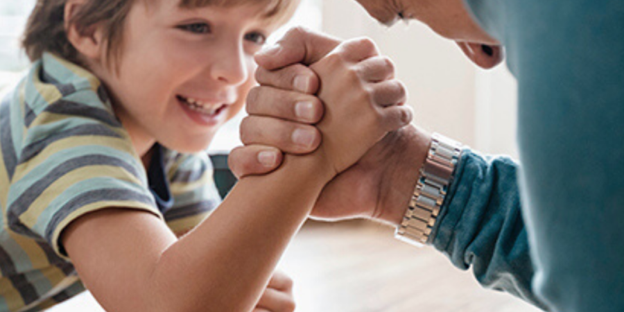 Boy and man arm wrestling playfully.