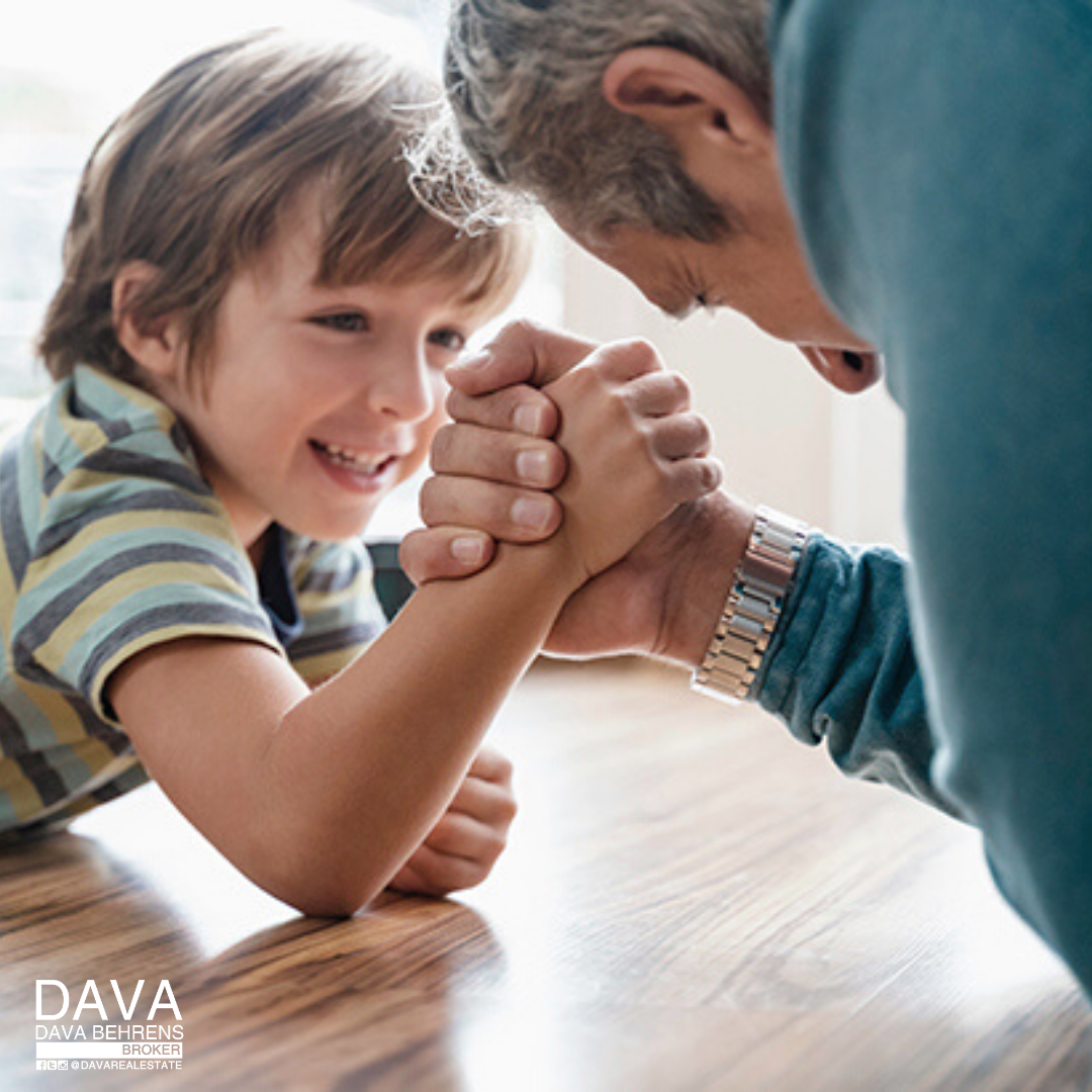 Boy and man arm wrestling playfully.