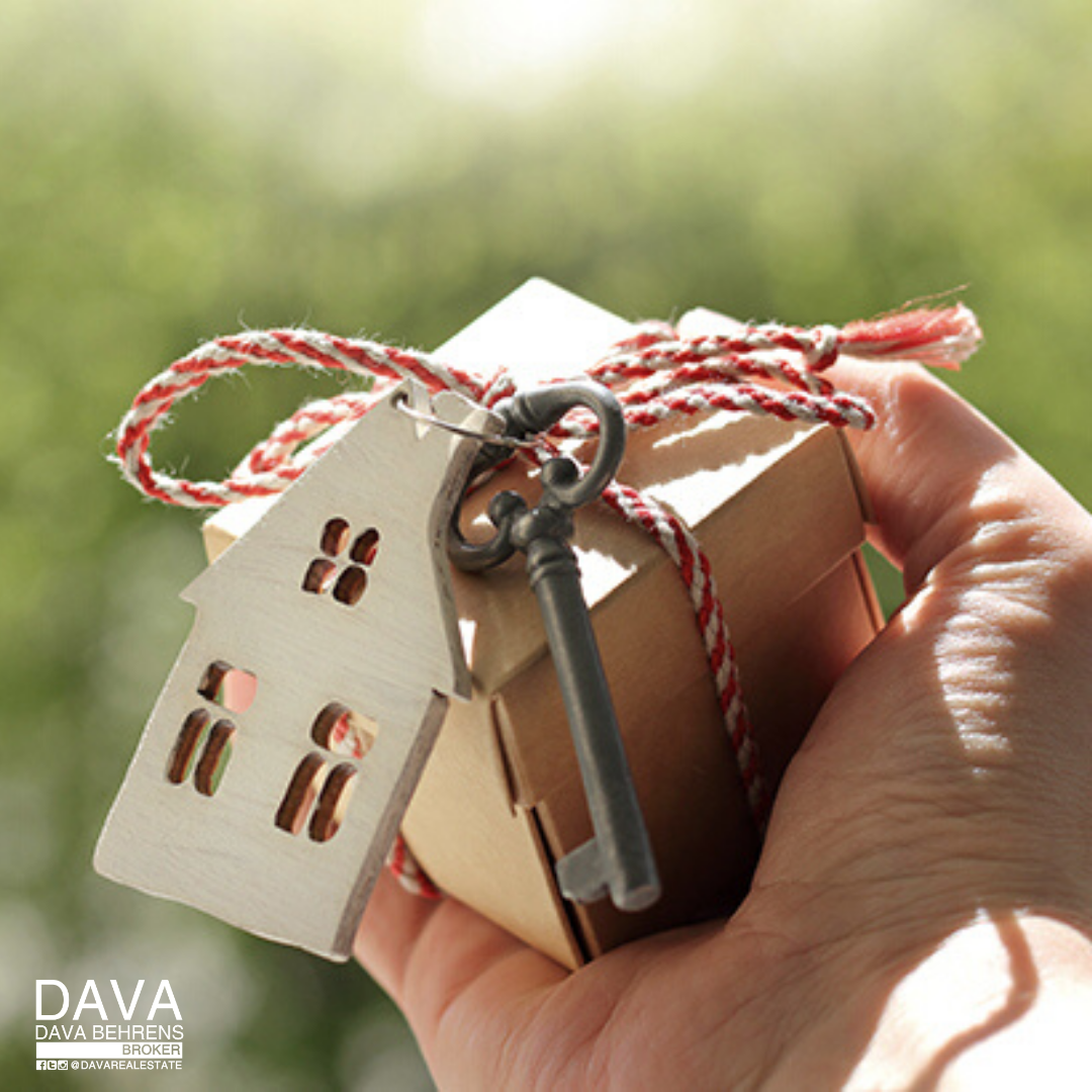 Hand holding house-shaped key and gift.