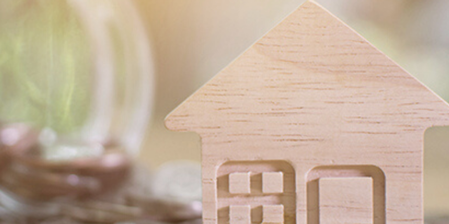 Wooden house model on coins, saving for home.