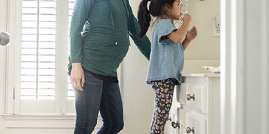 Pregnant mom helps daughter brush teeth.