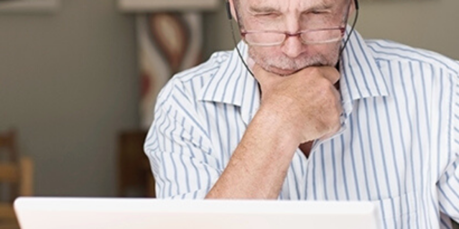 Man in glasses using laptop, thinking.