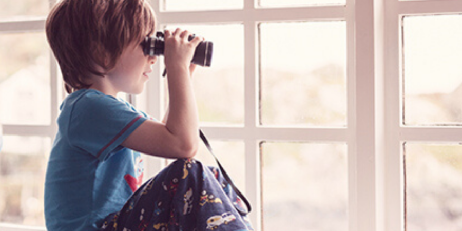 Boy using binoculars by window.