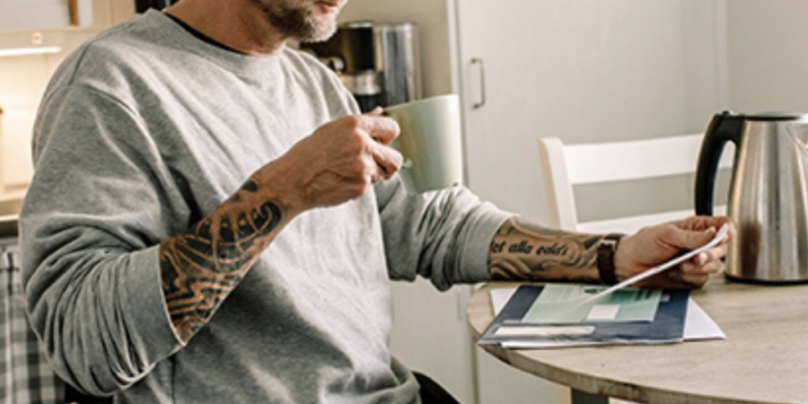 Man in wheelchair reviewing paperwork with coffee.