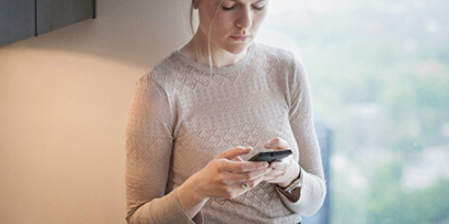 Woman texting in kitchen near window.