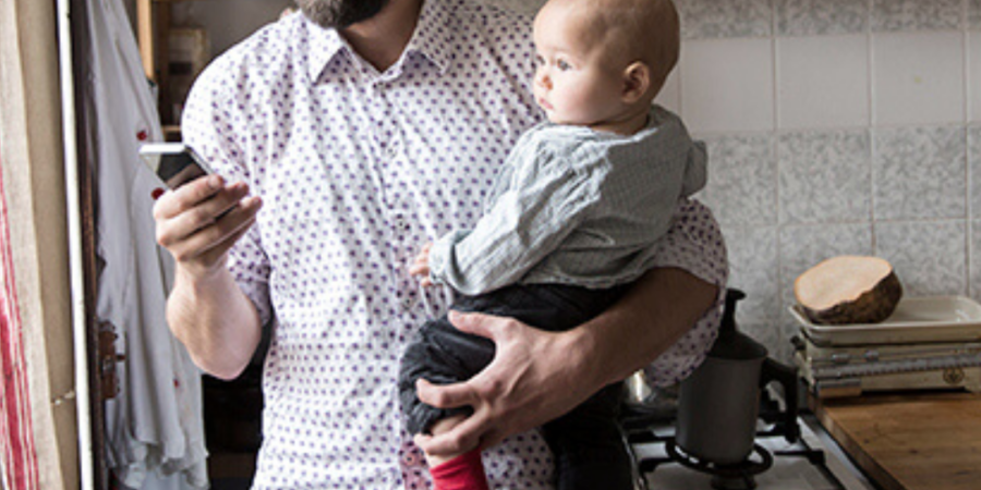 Father holding baby, checking phone.