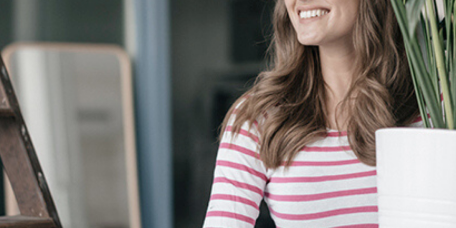 Woman smiling, holding potted plant.