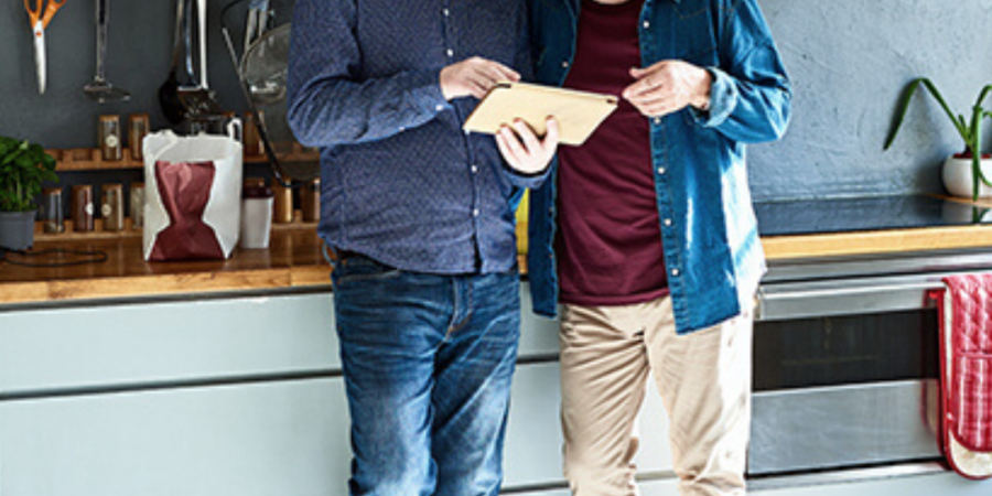 Two men reviewing a tablet in a kitchen.