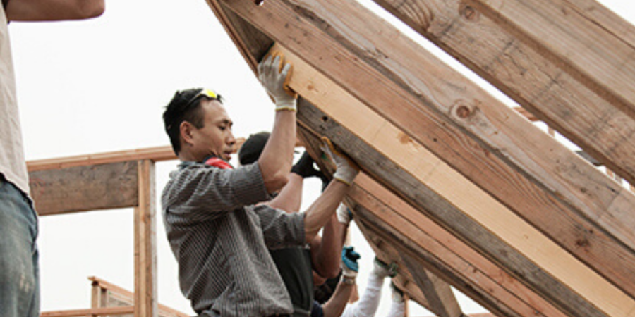 Workers installing roof beams on house.