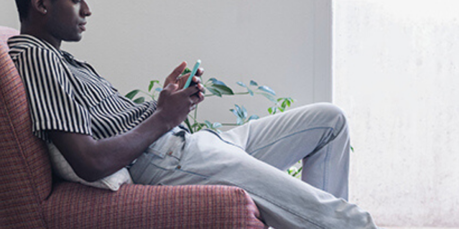 Man relaxing, using phone on armchair.