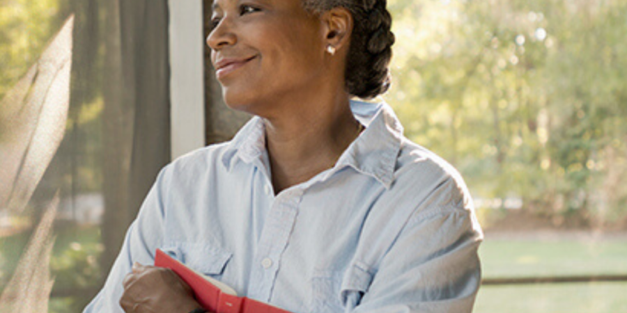 Woman holding book, looking out window.