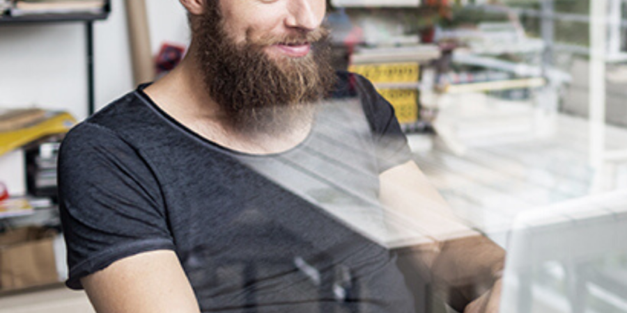 Man with beard working on laptop.