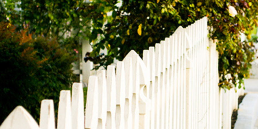 White picket fence beside green bushes.