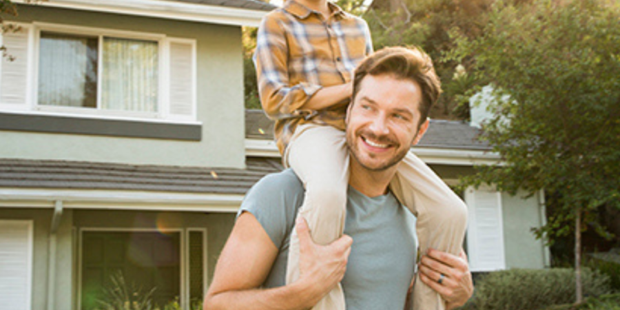 Father carrying son in front of house.