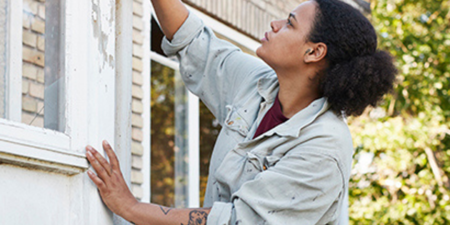 Woman sanding paint from window frame.