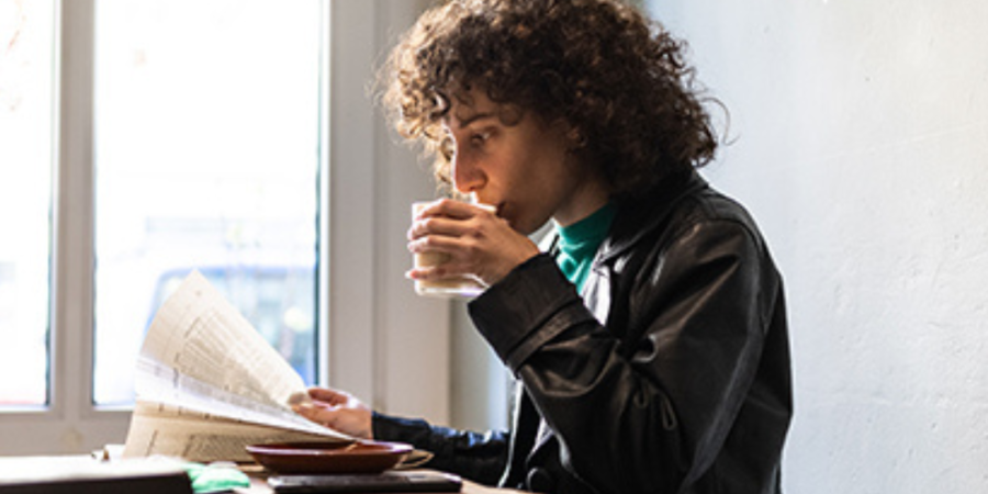 Woman reading newspaper, drinking coffee.