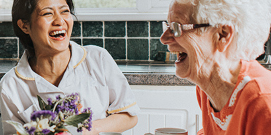 Happy caregiver and senior woman enjoying tea.