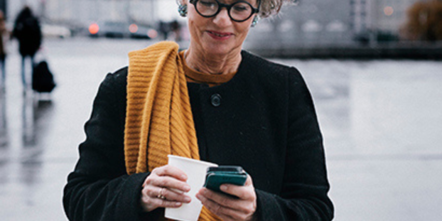 Woman using phone, coffee in hand.