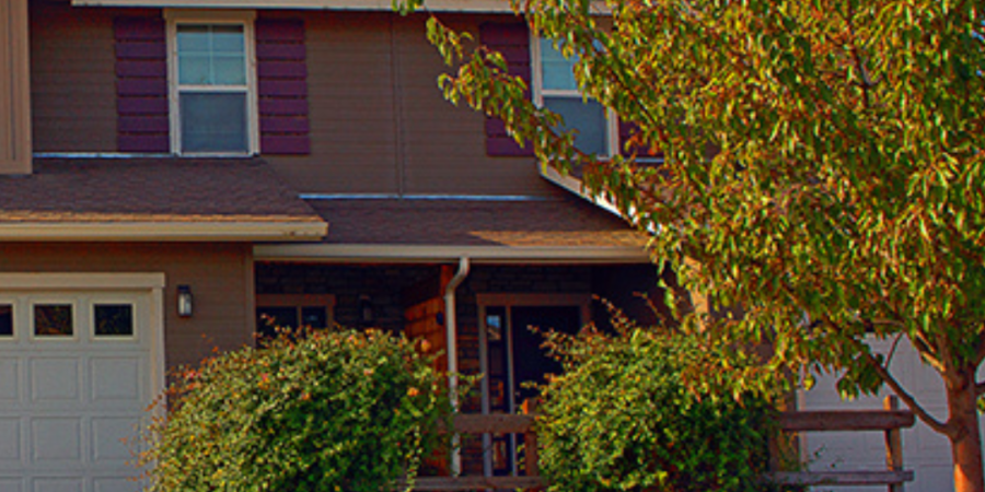 Brown townhouse with garage and shrubs.