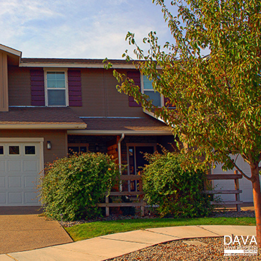 Brown townhouse with garage and shrubs.