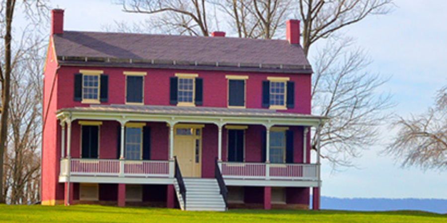 Red historic house on green lawn.