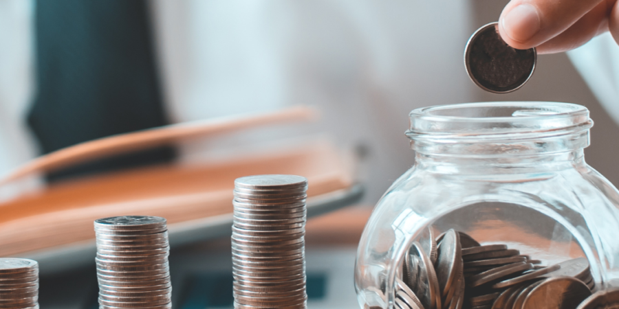 Person saving coins in glass jar.