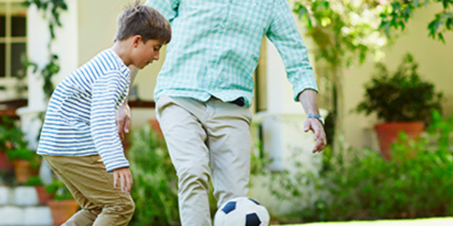 Father and son playing soccer in yard.