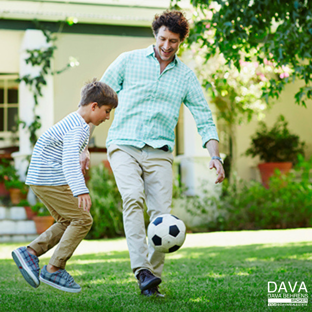 Father and son playing soccer in yard.