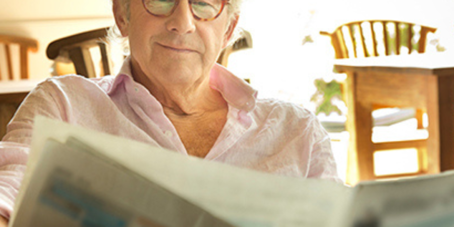 Senior man reading newspaper indoors.