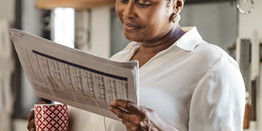 Woman reading newspaper with coffee.