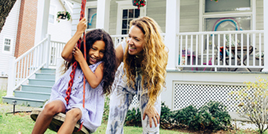 Mom and daughter playing on swing in front yard.