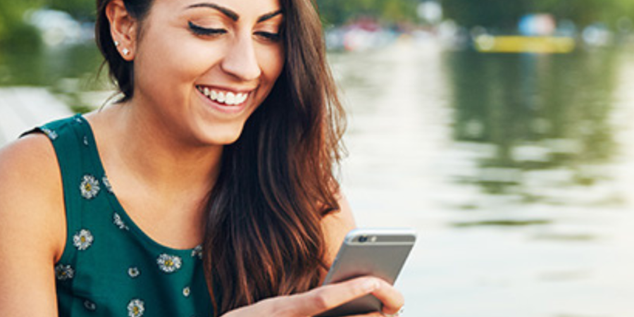 Woman smiling, using smartphone by lake.