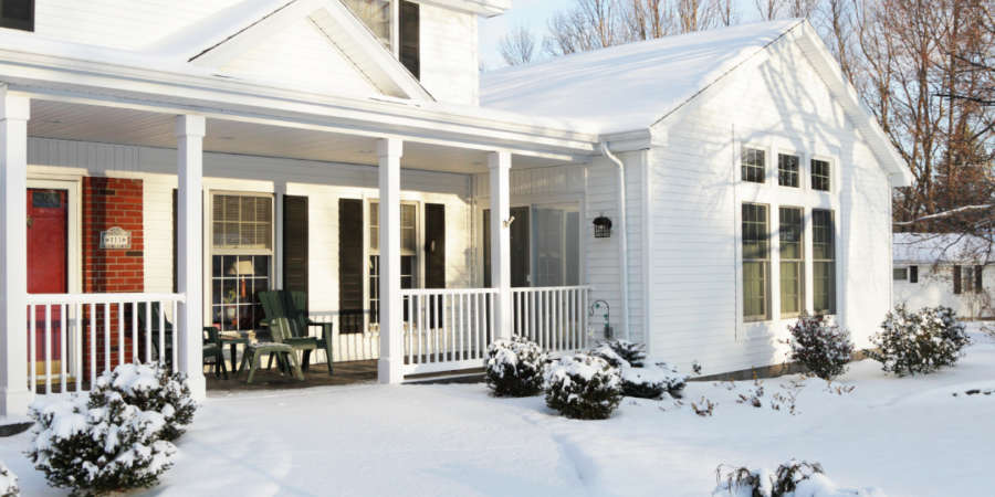 Snowy white house with porch and snow.