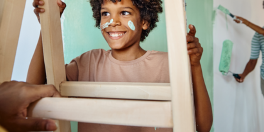 Child painting, smiling on ladder.