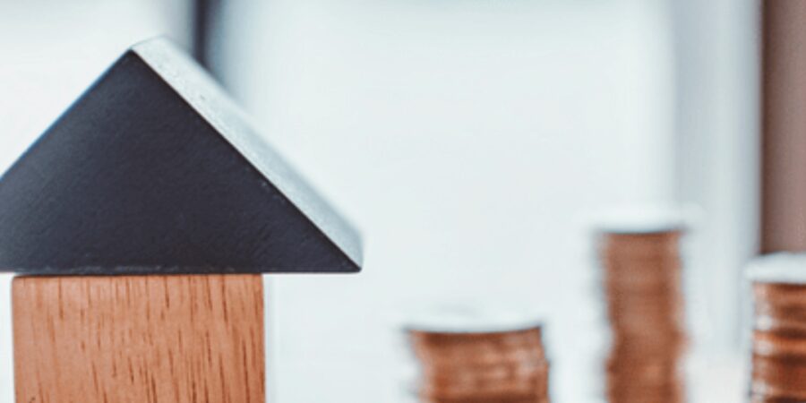 Wooden house model next to stacked coins.
