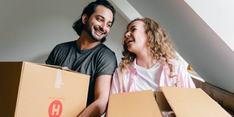 Couple smiling while carrying moving boxes.