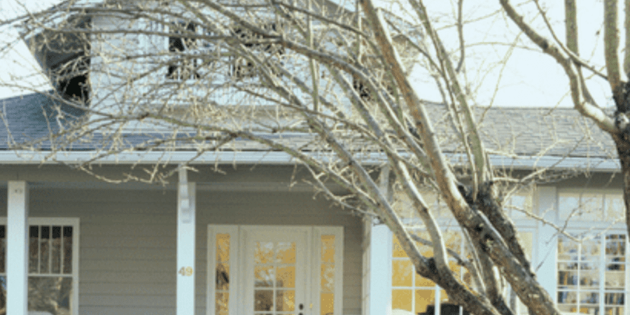 Gray house with white porch and tree.