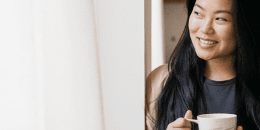 Woman smiling, holding coffee by window.