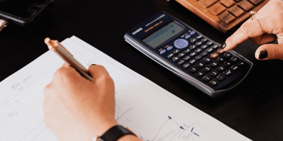 Person calculating finances with calculator and pen.