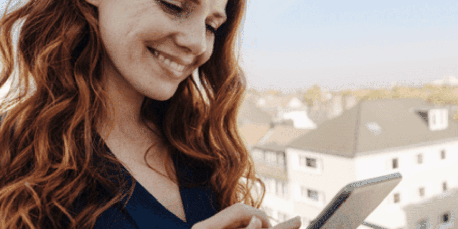 Woman smiling while using a tablet outdoors.