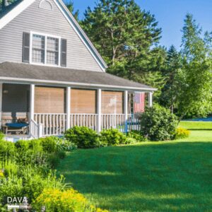 Gray house with porch and lush greenery.