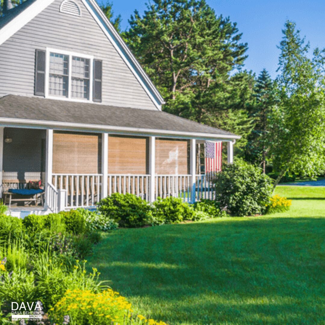 Gray house with porch and lush greenery.